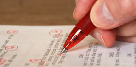 A hand holding a red pen, marking proofreader's symbols and abbreviations on a screenplay